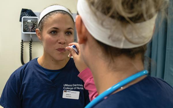 Nursing student places thermometer in another nursing student's mouth