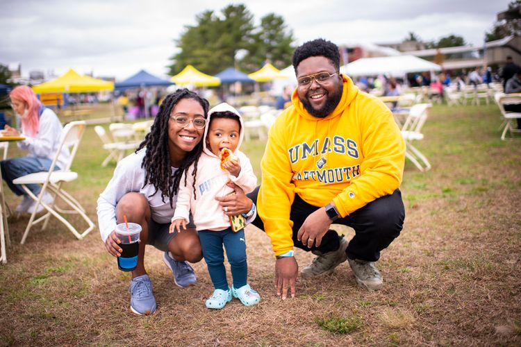 A man and woman stand with their child and smile at the camera