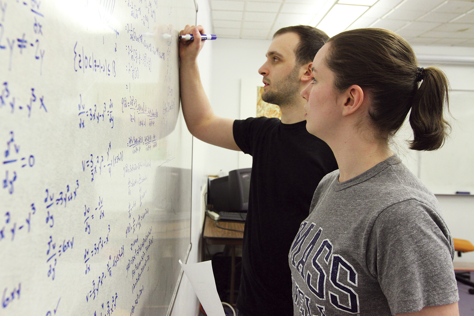 Two students write on whiteboard in classroom