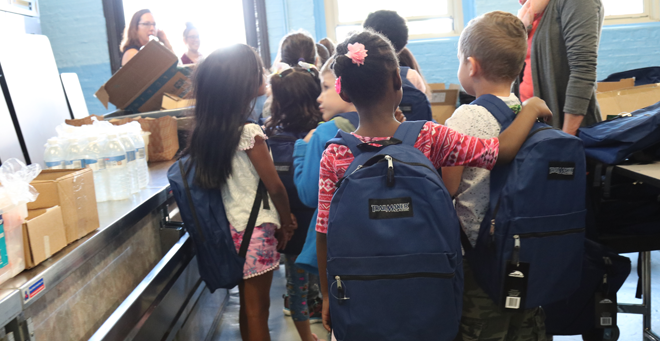 Elementary school students wait in line with backpacks on