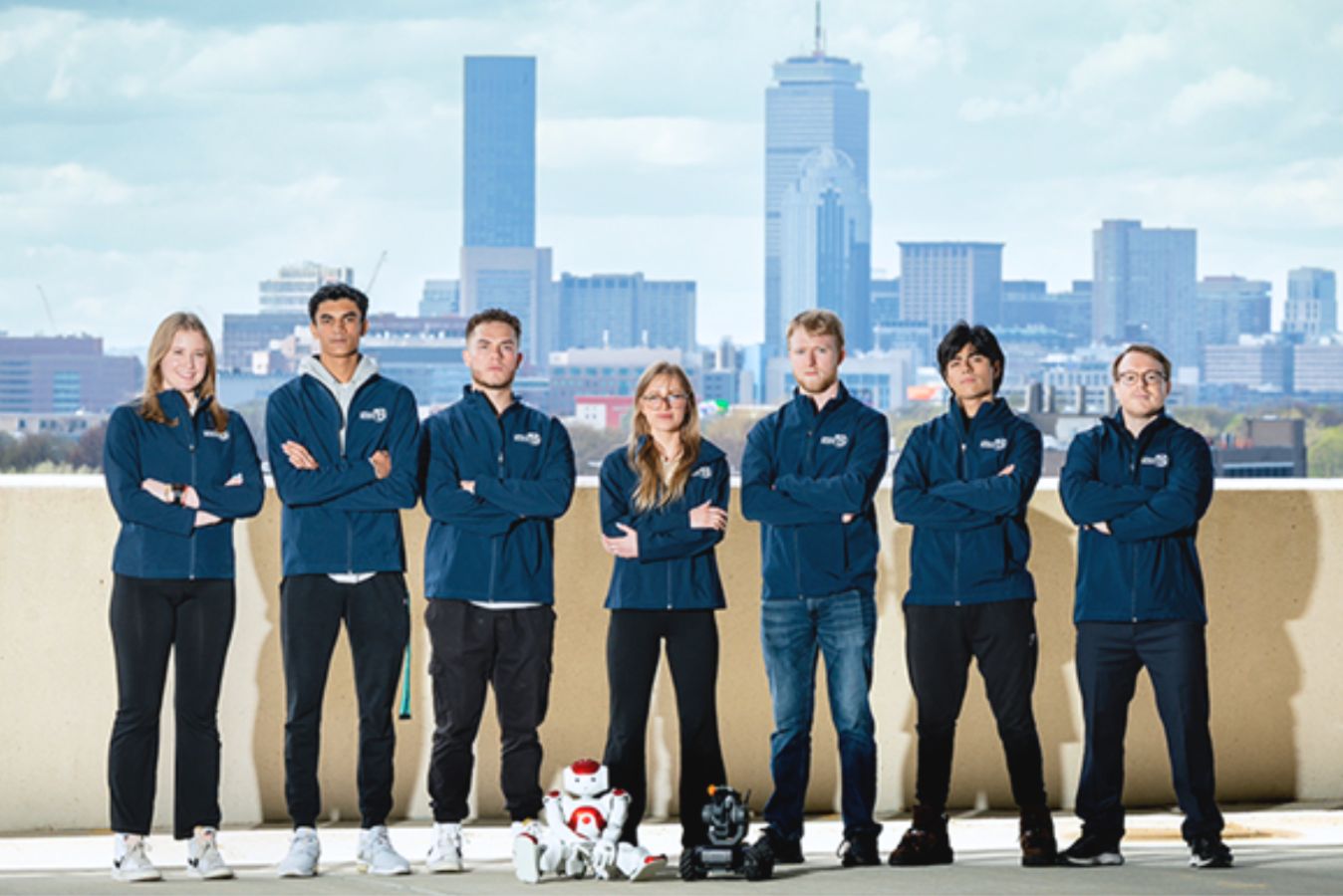 UMass Boston's Robotics and Engineering Club in front of the Boston city skyline.