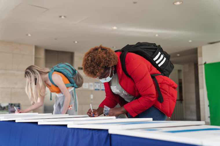 Students write why they are proud to be First Gen on a canvas that will be displayed in the Campus Center. Photo by Janina Seibel.