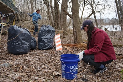 Senior environmental science major Fiona Benzi collects litter along the riverbank while Brad Buitenhuys, executive director of Lowell Litter Krewe, moves a large piece of trash in the background.