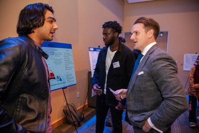 Business majors Madhav Makadia, left, and Kofi Kissi tell Assoc. Prof. Neil Shortland, who emceed the Idea Challenge, about their DifferenceMaker project.