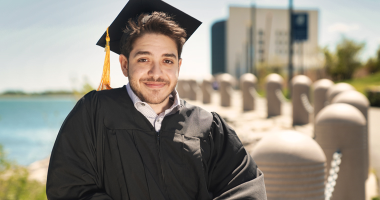 Hakeem Alhady wearing commencement gown and cap on UMass Boston campus