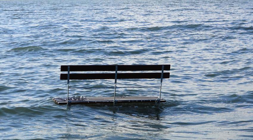 Half of a bench is seen on a beach with the bottom half underwater due to high sea level