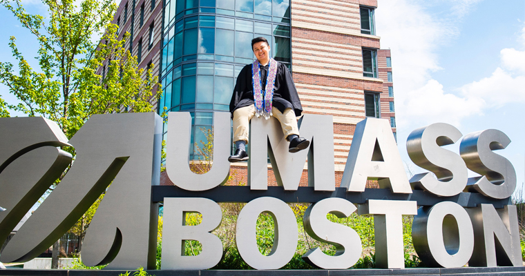 MG Xiong sits on top of UMass Boston sign