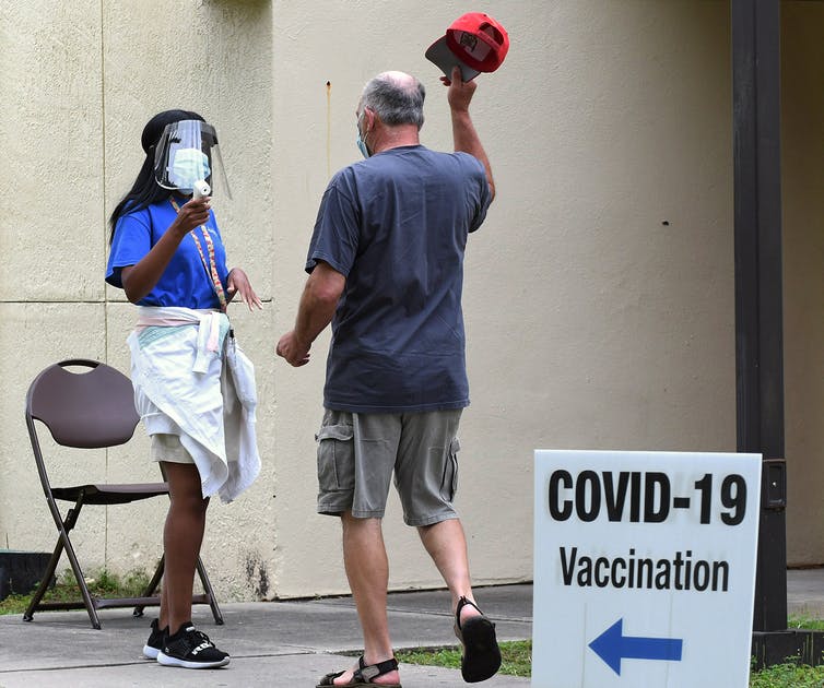 COVID Vaccine site volunteer directs man to entrance after taking his temperature