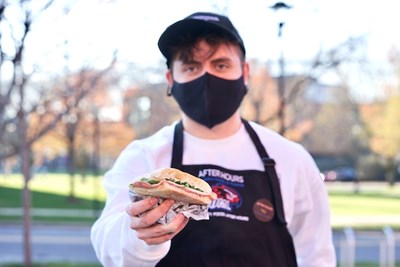 Senior business student Alec Itzaina holds up a panini from After Hours, a student-run business he helped create in his Internship for Entrepreneurship course.