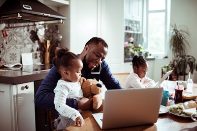 A father works on his computer while his two daughters sit next to him.