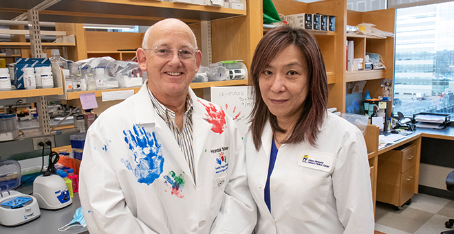Jason Shohet, MD, PhD, sporting a white coat with handprints of cancer survivors treated at UMass Memorial Medical Center, with research collaborator Joae Qiong Wu, PhD.