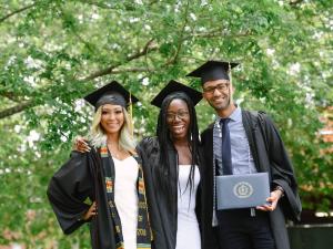  Three UMass Boston students at graduation standing together in a group photo smiling.