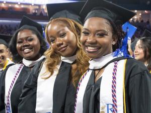 UMass Lowell graduates smiling at the 2023 commencement wearing their robes and caps.