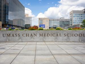 UMass Chan Medical School sign on a curved wall with the campus in the background on a warm summer day. 