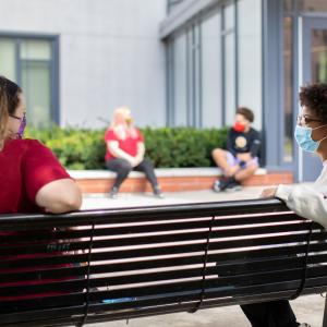 Two masked students sit socially distant on a bench