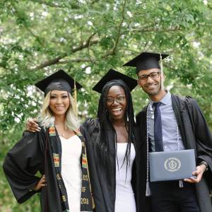  Three UMass Boston students at graduation standing together in a group photo smiling.
