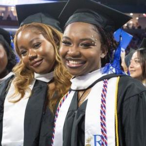 UMass Lowell graduates smiling at the 2023 commencement wearing their robes and caps.