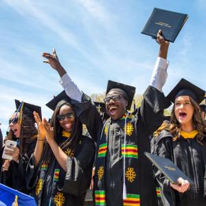 UMass Dartmouth students at commencement cheering in their regalia.