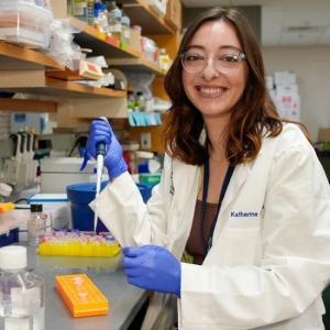 Woman in lab coat smiles at camera while using syringe. 