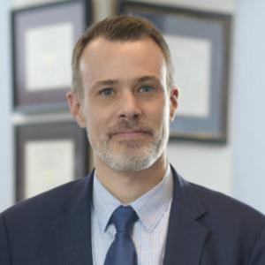 Headshot of David McManus, man with grey beard, brown hair wearing a suit and tie. 