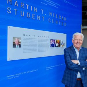 President Meehan standing beside Martin T. Meehan Student center signage. 