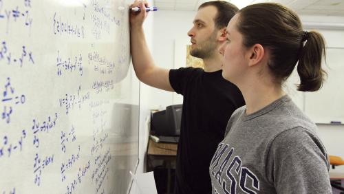 Two students write on white board in classroom