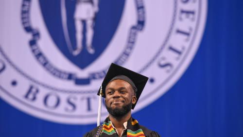 Student smiling on stage of UMass Boston commencement
