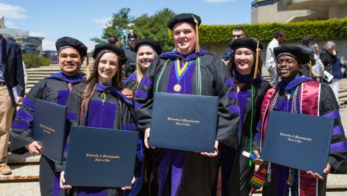 A group of UMass Law students smiling with their degrees after commencement ceremony