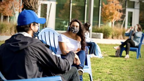 Two students sit outside on campus wearing masks