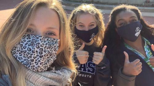 Three students smile at camera while wearing masks