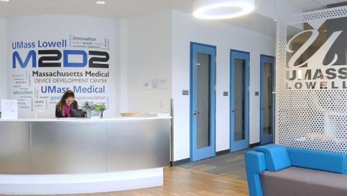 Interior of the UMass Lowell M2D2 building with a female student sitting behind the reception desk