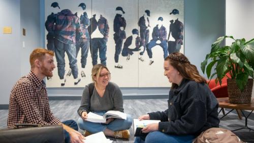 Three students sitting on the floor with open textbooks, talking.