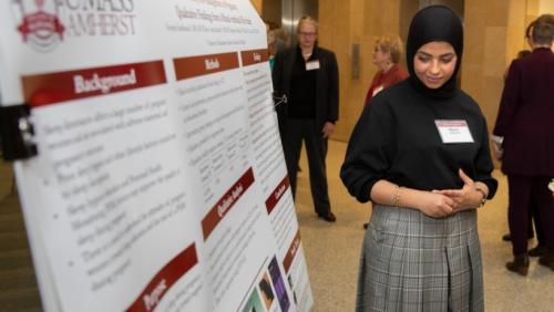 Student presenting a poster with people standing in the background.